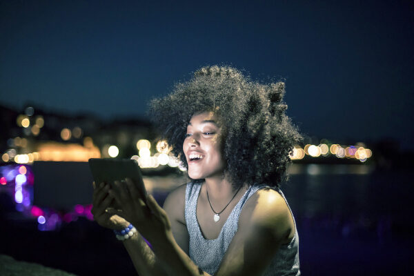 Cheerful woman using digital tablet on beach at night Business Broadband